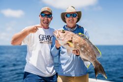 two men in hats and sunglasses posing with large caught fish on boat