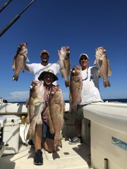 Three men in hats posing with large caught fish on boat
