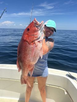 Woman on a boat holds a large red snapper fish with the ocean and blue sky in the background.