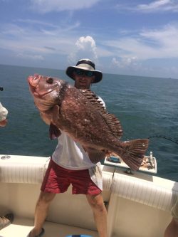 Person on a boat holding a large fish with the ocean and sky in the background.