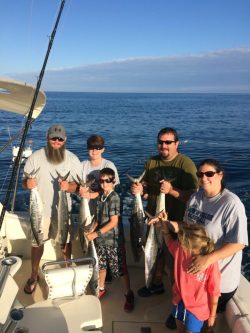 Five people on a boat hold up large fish they caught, with the ocean and blue sky in the background.