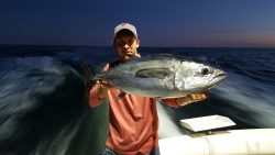 Person on a boat holding a large fish with the ocean and dark sky in the background.