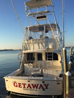 White fishing boat named "Getaway" docked at a marina in Orange Beach, Alabama, with fishing gear on board.