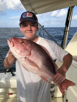 Person on a boat holding a large red snapper fish with the ocean in the background.